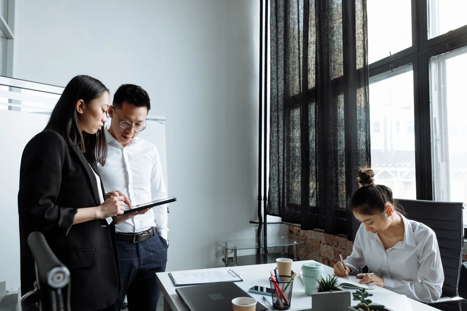 Three colleagues working together with a tablet and written records in a bright office